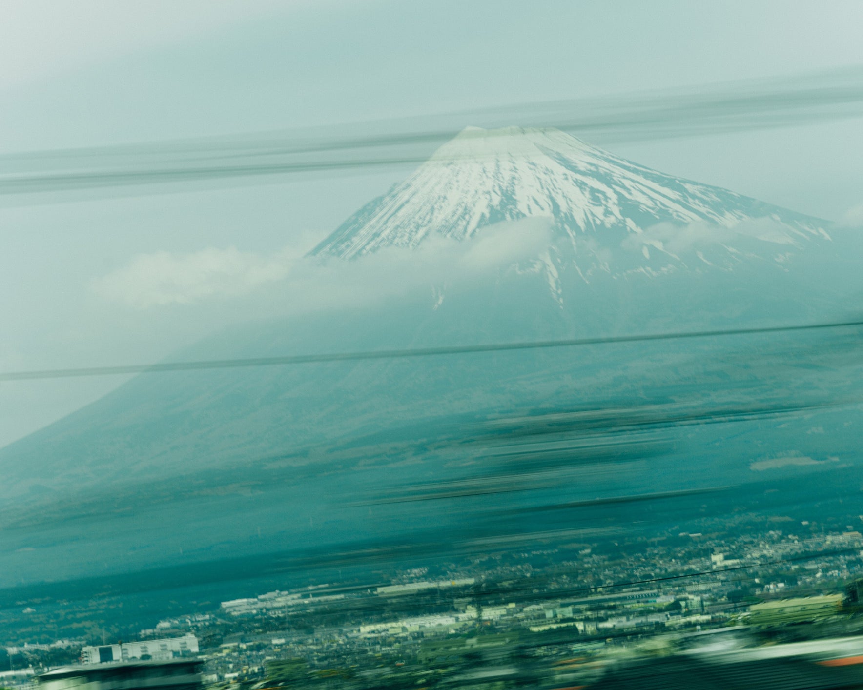 A blurred image of Mount Fuji, its snow-capped peak towering above the landscape, as seen through a moving window, capturing a fleeting yet majestic view of Japan’s iconic mountain.