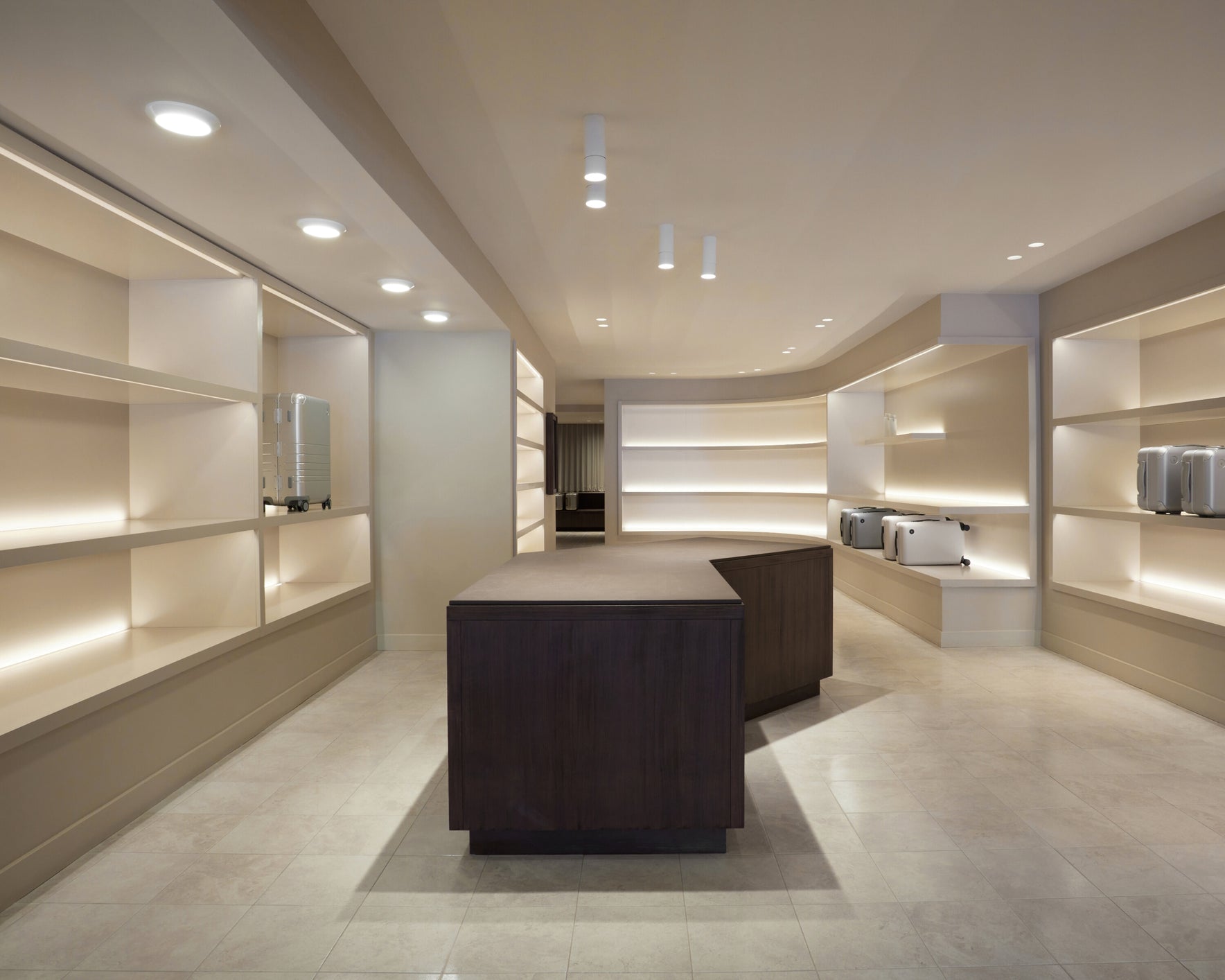 Monos Boston store interior with illuminated shelving and silver luggage displayed in a minimalist space.