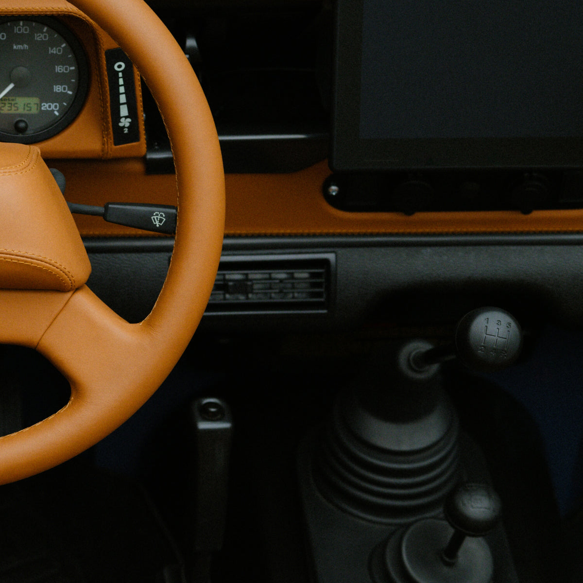 Close-up of the tan leather interior and steering wheel of the custom Arles Blue Land Rover Defender 90, highlighting the dashboard and gear shift details.