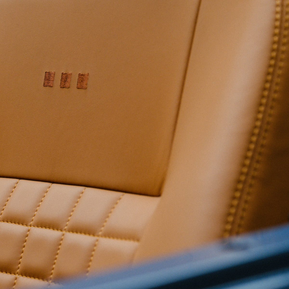 Close-up of the tan leather seat in the custom Arles Blue Land Rover Defender 90, featuring quilted stitching and subtle embroidered detailing.