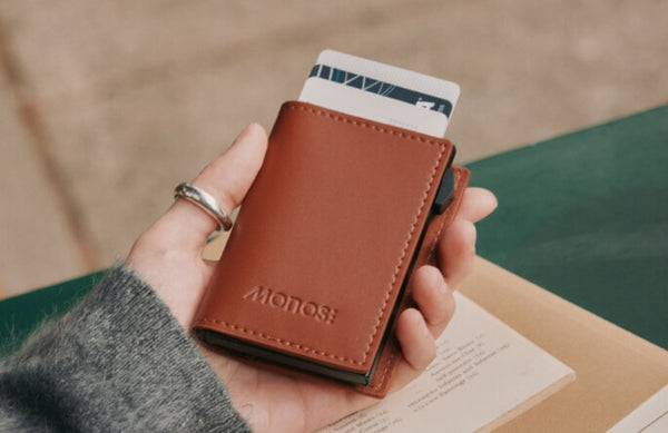 A hand holding a Monos Slim Wallet Pro in Mahogany / Black with cards partially visible at the top.