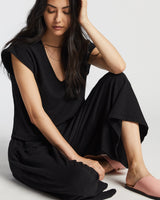 A woman sitting cross-legged on the floor of a studio, wearing a sevilla top and sevilla pants in black.