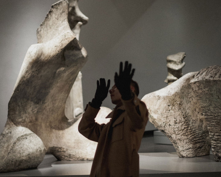 A person raises their hands in front of abstract sculptures in a museum, evoking a sense of awe and interaction with the art.