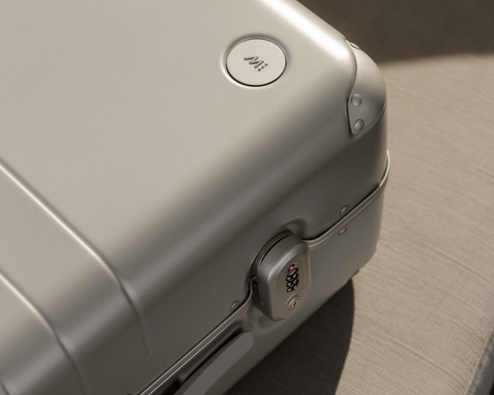 A close-up of a hybrid carry-on in silver, focusing on the Monos logo and built-in TSA-accepted lock, capturing the durable and elegant finish.