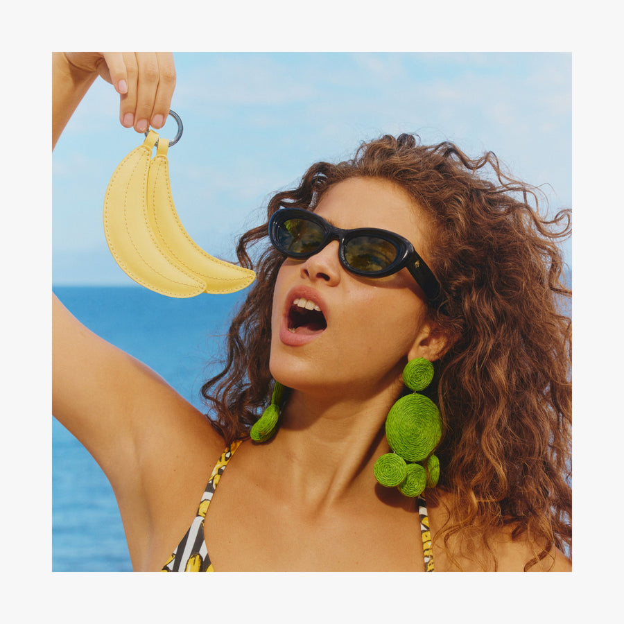 Banana | Woman standing by the ocean holding a Banana Charm like she is eating it
