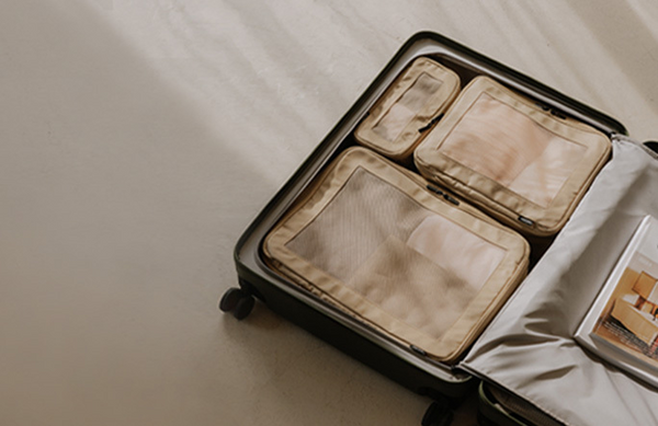 An open suitcase with neatly organized compressible packing cubes in Tan, placed on a light-colored floor with soft natural lighting.