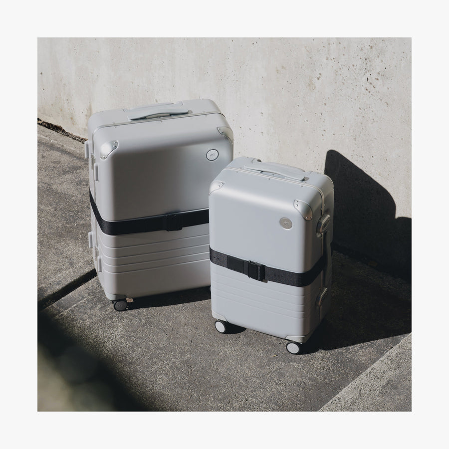 Ocean Blue | Front view of two different sizes of Aluminum suitcases on the street with the Midnight Black Luggage Strap secured around them