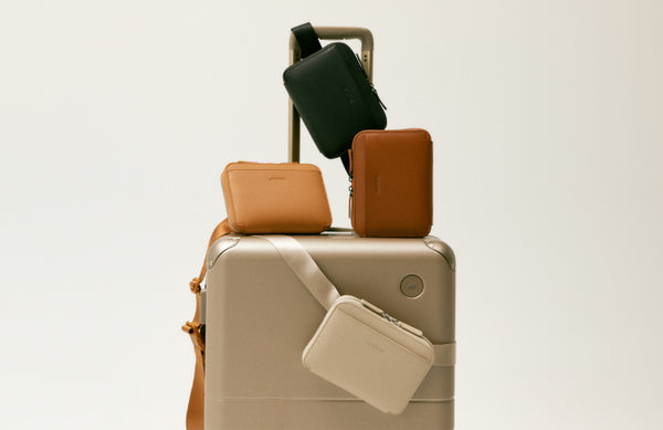 A collection of metro belt bag in various colours, attached to a hybrid carry-on in champagne with an extended handle.