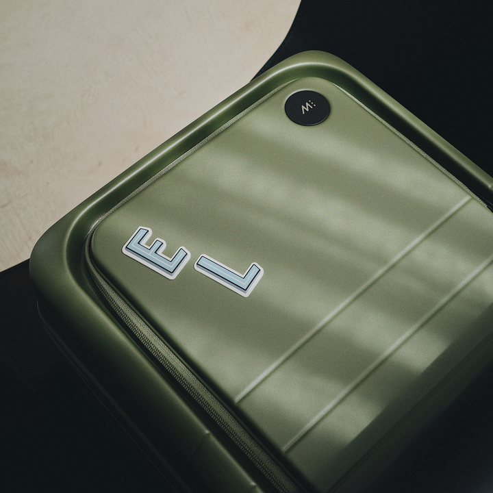 The Monos Carry-On Pro in olive green, customized with Alphabet Stickers on the front pocket.