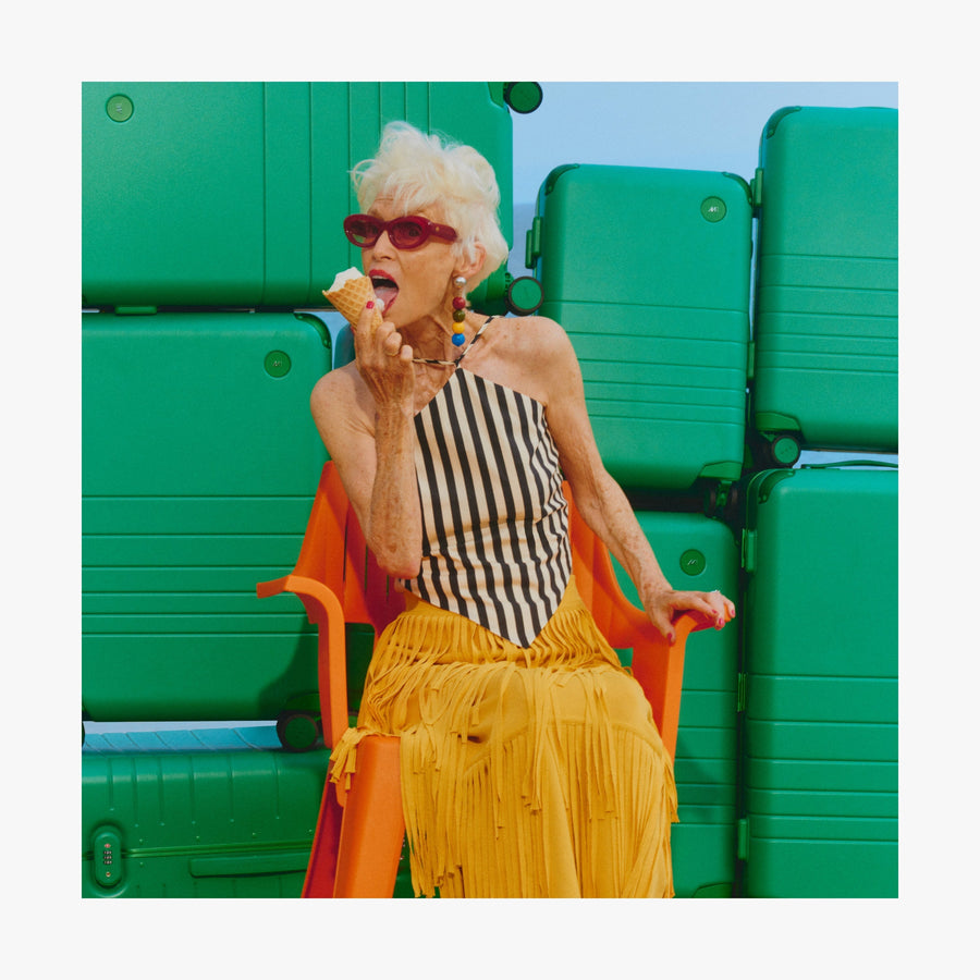 Jungle Green | Woman eating ice cream in front of a stack of Jungle Green Hybrid suitcases in different sizes