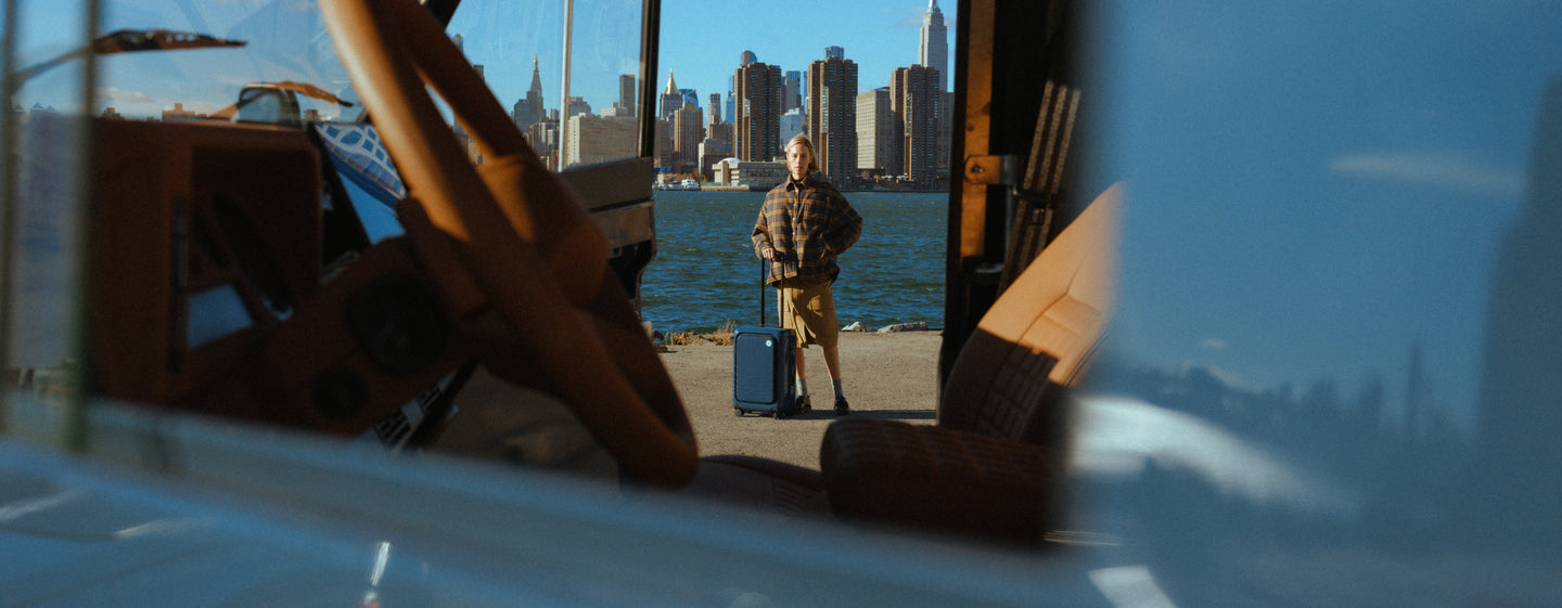 Person with a suitcase standing on a dock with a city skyline in the background