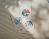 Destination Stickers by Monos, featuring New York, London, and Los Angeles designs, displayed on cream cards in soft sunlight.