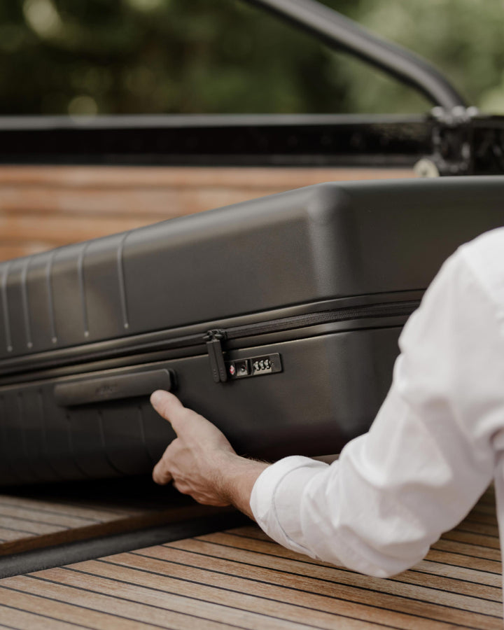 A person places a Check-In Large in Midnight Black into the car, with the side fixed handle facing up and the TSA lock visible.