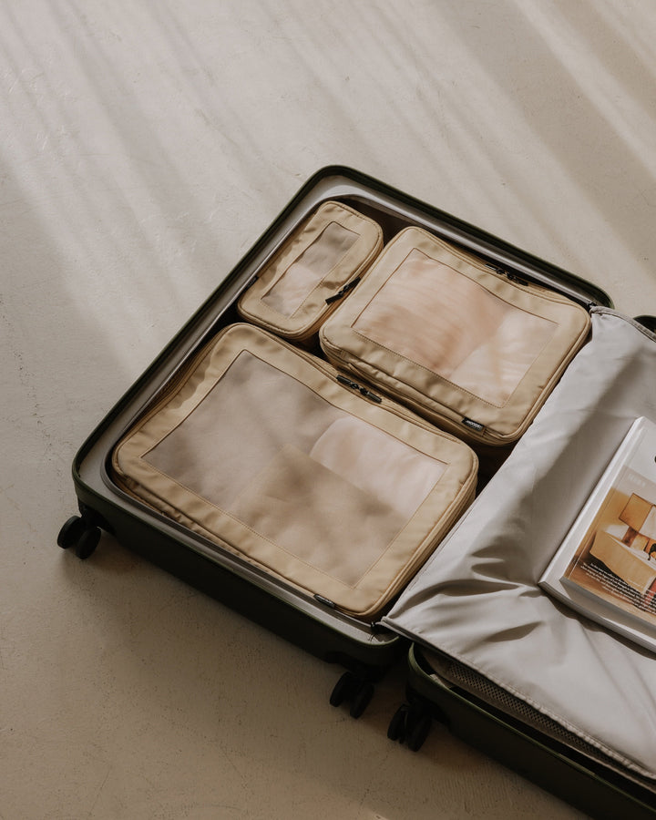 An open Monos suitcase reveals neatly packed Set of four Compressible Packing Cubes in Tan, arranged efficiently inside the main compartment.