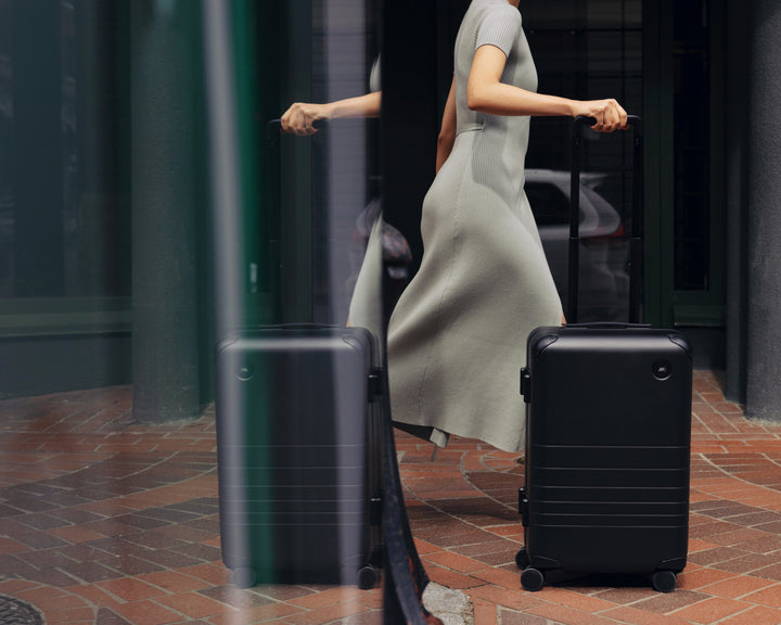 A woman in motion with a Hybrid Carry-On in Obsidian in the foreground.