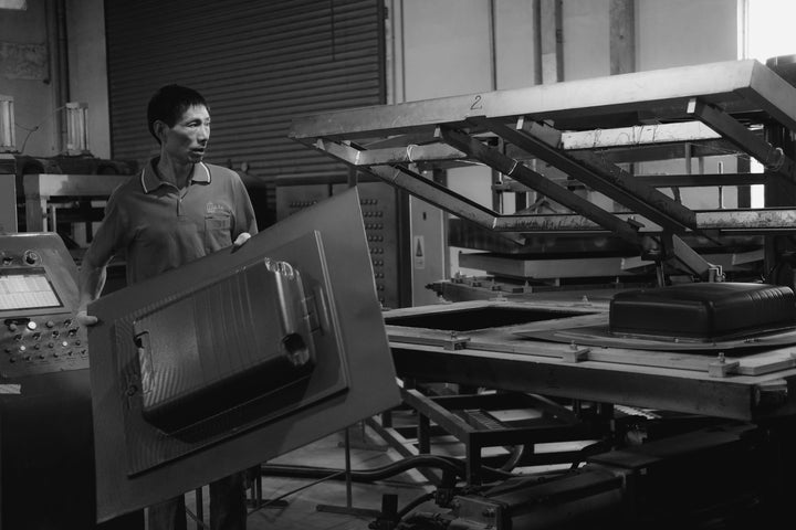 An operator removes a freshly molded Monos luggage shell from a vacuum-forming machine inside the factory.