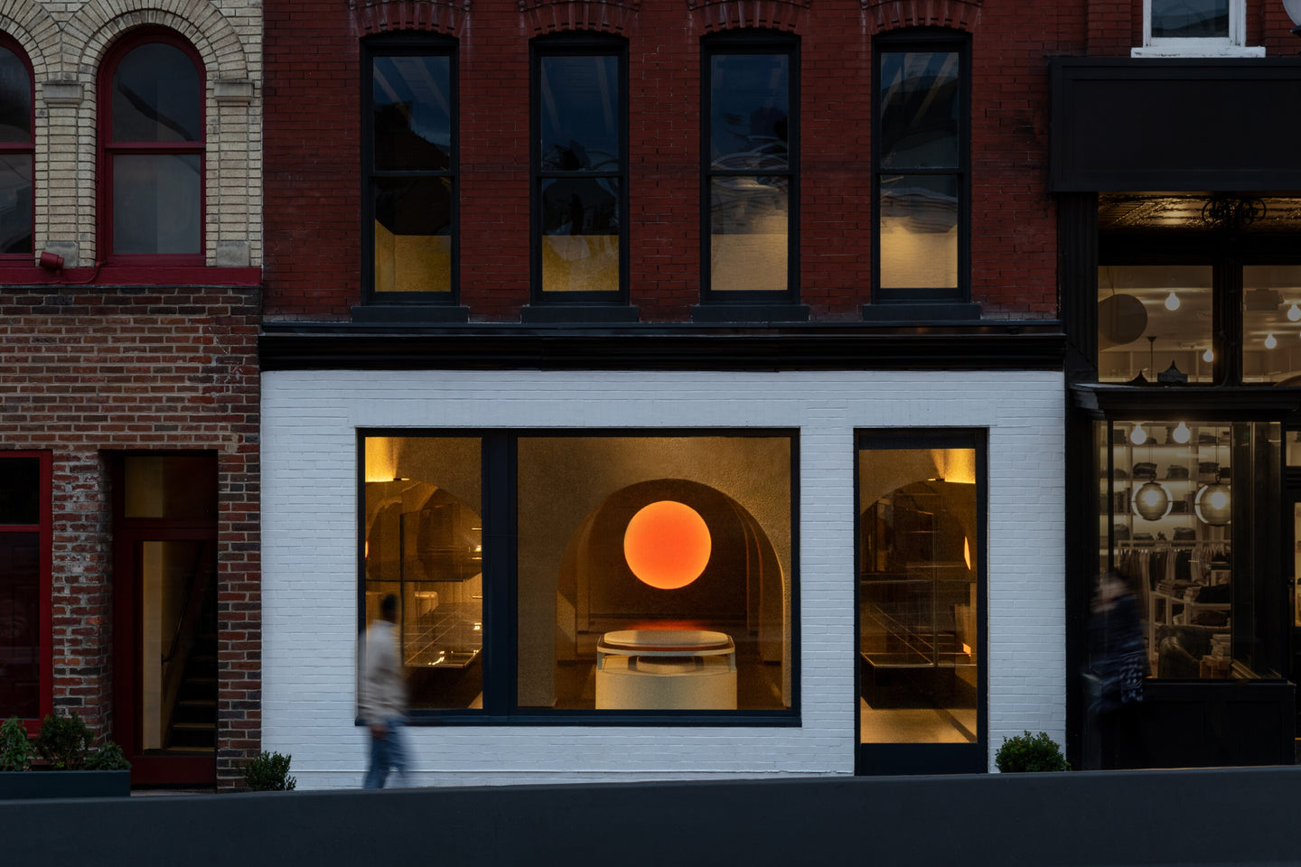 Monos Georgetown store exterior in Washington, D.C., featuring minimalist design and a glowing circular light visible through large windows.