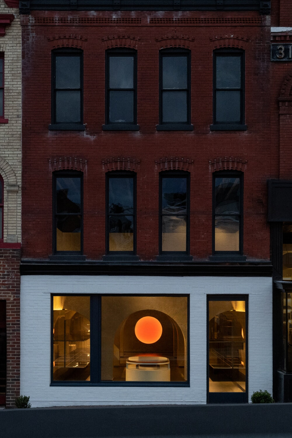 Monos Georgetown store exterior in Washington, D.C., featuring minimalist design and a glowing circular light visible through large windows.