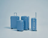 Four Hybrid suitcases of different sizes in Elemental Blue stand against a light blue background.