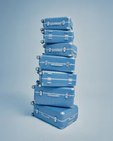 A tall stack of Hybrid suitcases in Elemental Blue is neatly balanced against a light blue background.