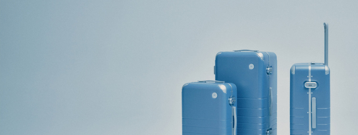 Three Hybrid suitcases of different sizes in Elemental Blue stand against a light blue background.