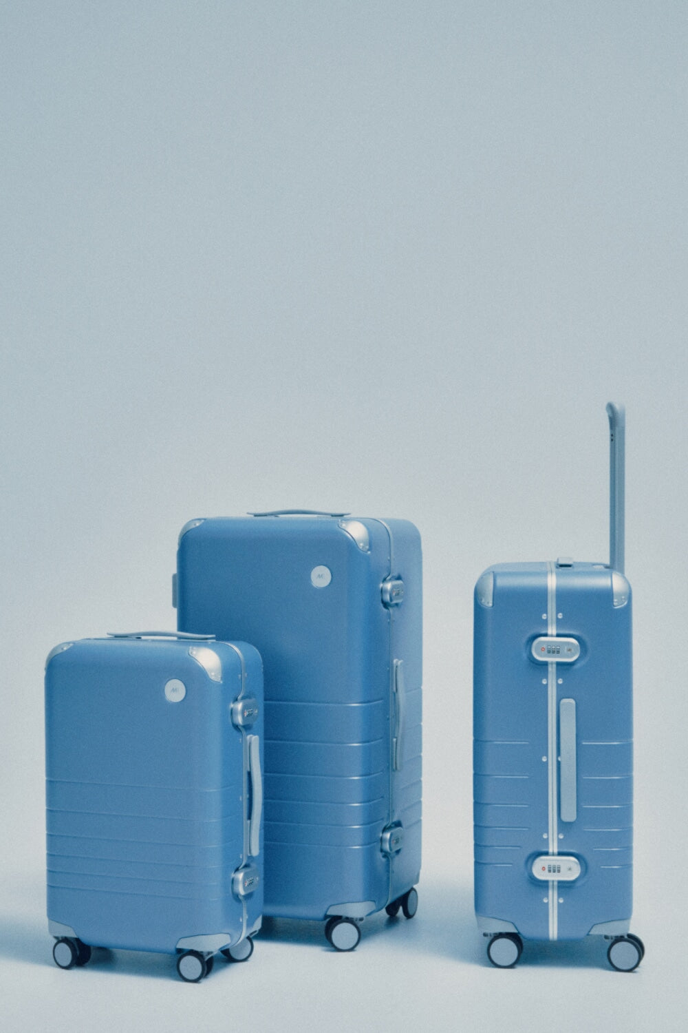 Three Hybrid suitcases of different sizes in Elemental Blue stand against a light blue background.