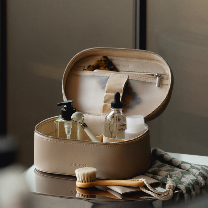 Metro Cosmetic Case in Ivory (Vegan Leather) is open, neatly filled with skincare bottles and tools, accompanied by a brush and a towel.