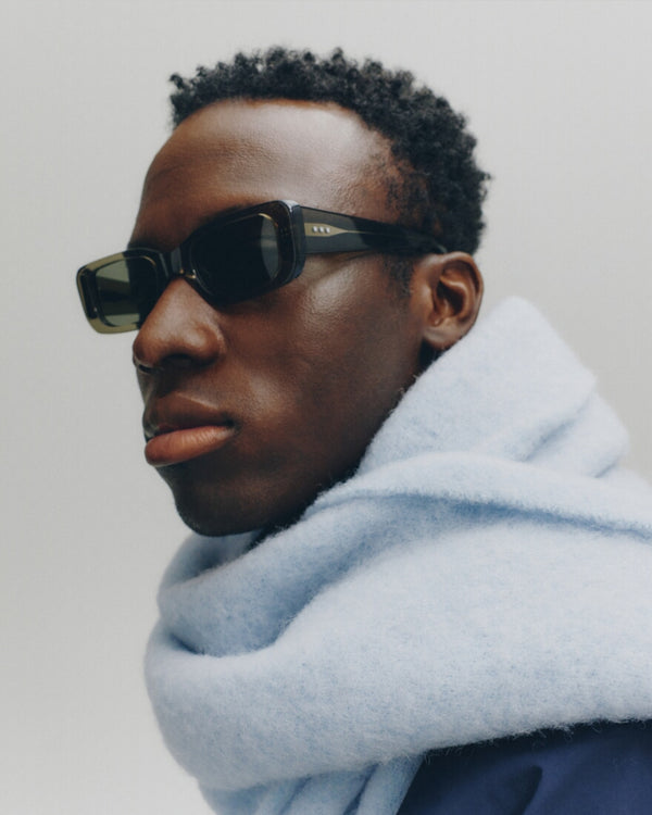 Person wearing sunglasses and a light blue scarf on a plain background