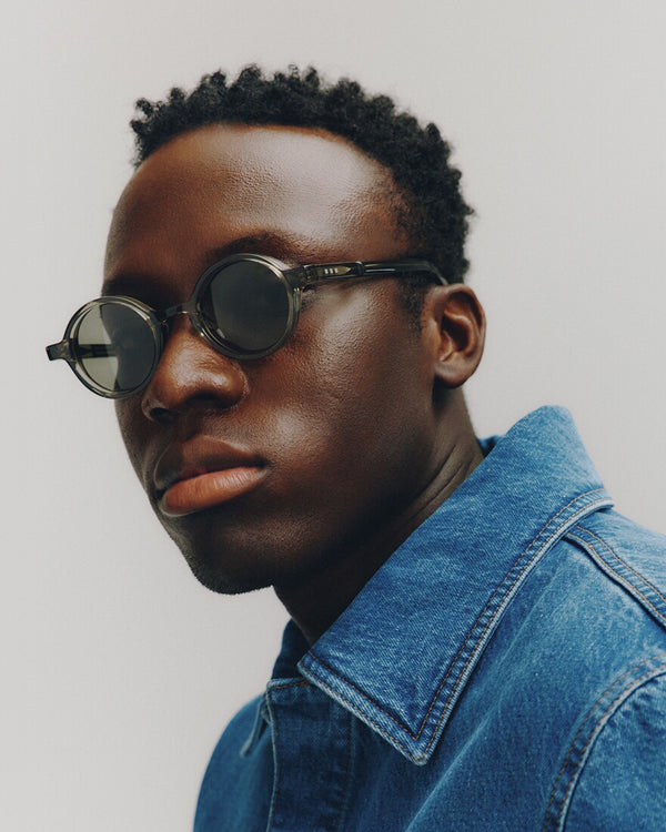 Man wearing sunglasses and a denim jacket against a plain background