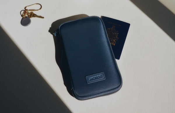 The Metro Travel Wallet in Oxford Blue, shown on a white surface with a passport and keys nearby.