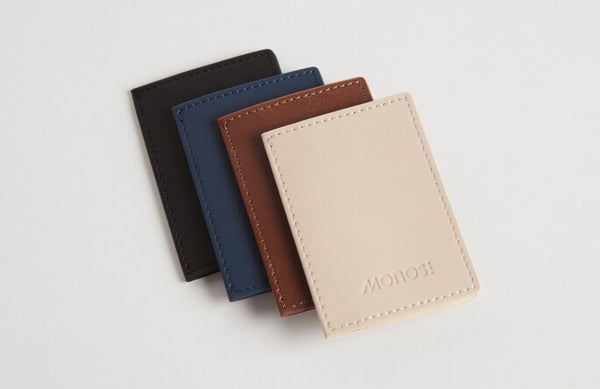 A lineup of four slim wallets in various colors—carbon black, oxford blue, mahogany, and ivory—displayed to highlight the color options and craftsmanship.