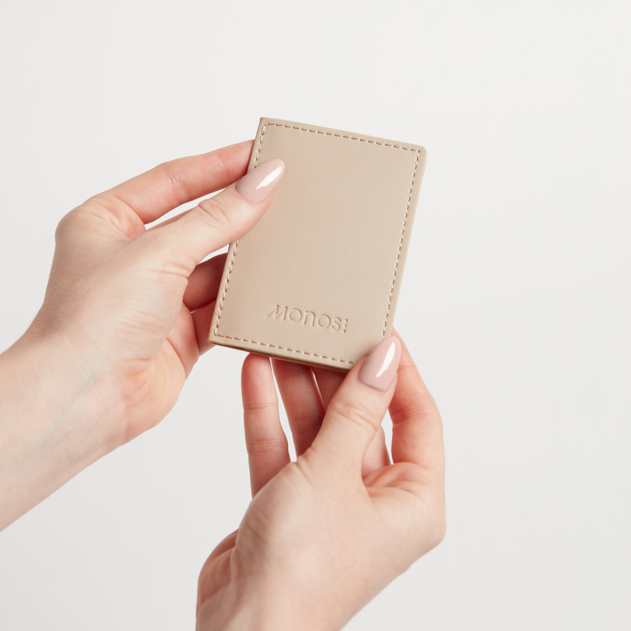 A close-up image of a person holding a Slim Wallet in Ivory with both hands, showcasing its minimalist design and embossed logo, set against a clean, white background.