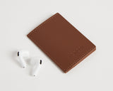 Slim wallet in Mahogany paired with white wireless earbuds, emphasizing the compact size and practicality of the wallet.