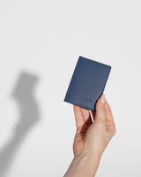 Slim wallet in Oxford Blue held in a person’s hand, with a shadow in the background, illustrating its lightweight and portable design.