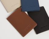 Four slim wallets in ivory, oxford blue, mahogany, and carbon black, arranged in a casual overlapping pattern to highlight the vegan leather material and stylish stitching.