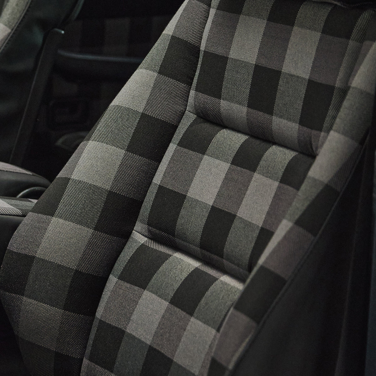 A close-up of a car seat cover with a black and gray buffalo plaid pattern, installed on a vehicle's front seat.