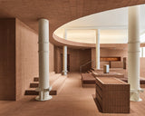 Spacious interior of the Monos SoHo store featuring terracotta brick walls, white columns, and tiered platforms with aluminum luggage under soft, diffused lighting.