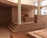 Sunlit interior of the Monos SoHo store featuring terracotta brick steps, white columns, and minimalist brass railings leading to a raised display area with warm wood accents.