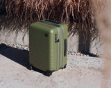 Monos Expandable Carry-On in Olive outdoors on sunlit concrete.