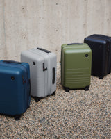 Lineup of Monos Expandable Carry-On suitcases in Ocean Blue, Storm Grey, Olive Green, and Midnight Black.
