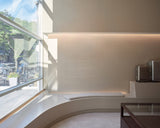 Monos Boston store interior with curved seating by a large front window and silver luggage displayed against a minimalist wall.