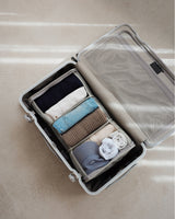 An open suitcase neatly packed with the Packable Hanging Closet, filled with folded essentials and travel basics, set against a sunlit neutral floor.