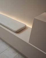 Detail of minimalist seating with a cushioned bench and soft backlighting inside the Monos Boston store.