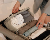 A close-up of the Packable Hanging Closet being lifted from a suitcase, neatly packed with rolled essentials, a knit sweater, and a travel cap.
