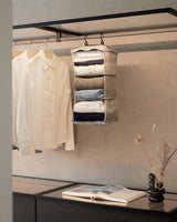 The Packable Hanging Closet suspended beside crisp white shirts in a modern wardrobe, with an open book and sculptural vase completing the calm, curated scene.