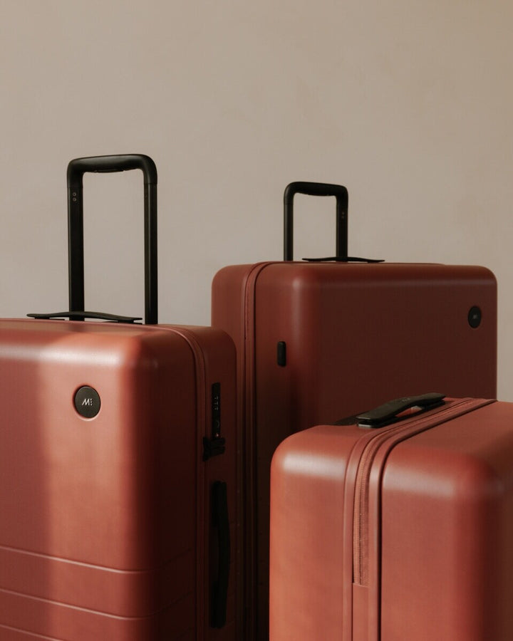 Three Monos suitcases in Terracotta stand side by side, with the telescopic handles extended and the Monos logo visible on the front.