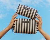 Two black and white striped bags held by hands against a blue sky.