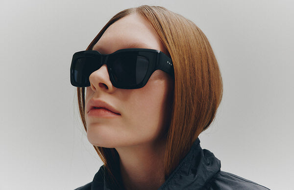 Mannequin head with sunglasses and a gray jacket on a plain background