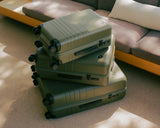 A stack of Olive Green suitcases of varying sizes, placed in a warm, inviting living room with natural light filtering through.