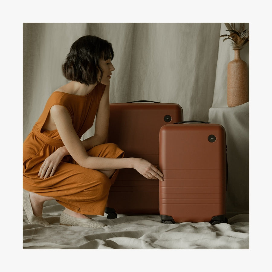 Terracotta | This is a photo of a woman kneeling beside the Terracotta Check-In and Carry-On Plus